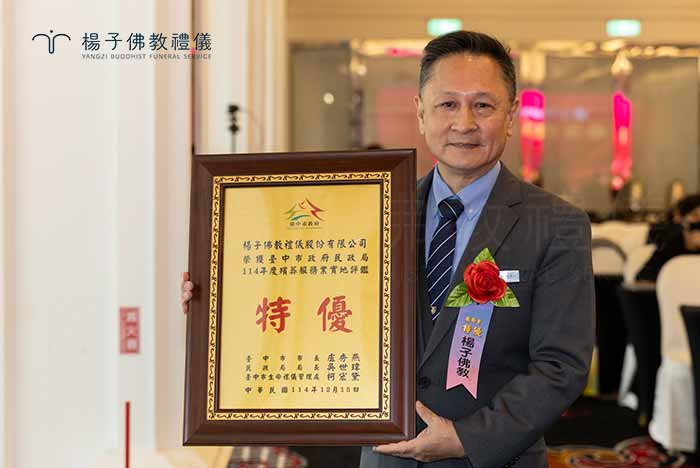 楊子佛教禮儀負責人楊子牧師兄，手持114年度台中市殯葬評鑑「特優」獎牌，自信展現團隊歷年累計連霸18座獎牌的輝煌紀錄。這不僅是榮譽，更是楊子堅持30年禮儀環保與優質服務的具體證明。｜楊子佛教禮儀公司